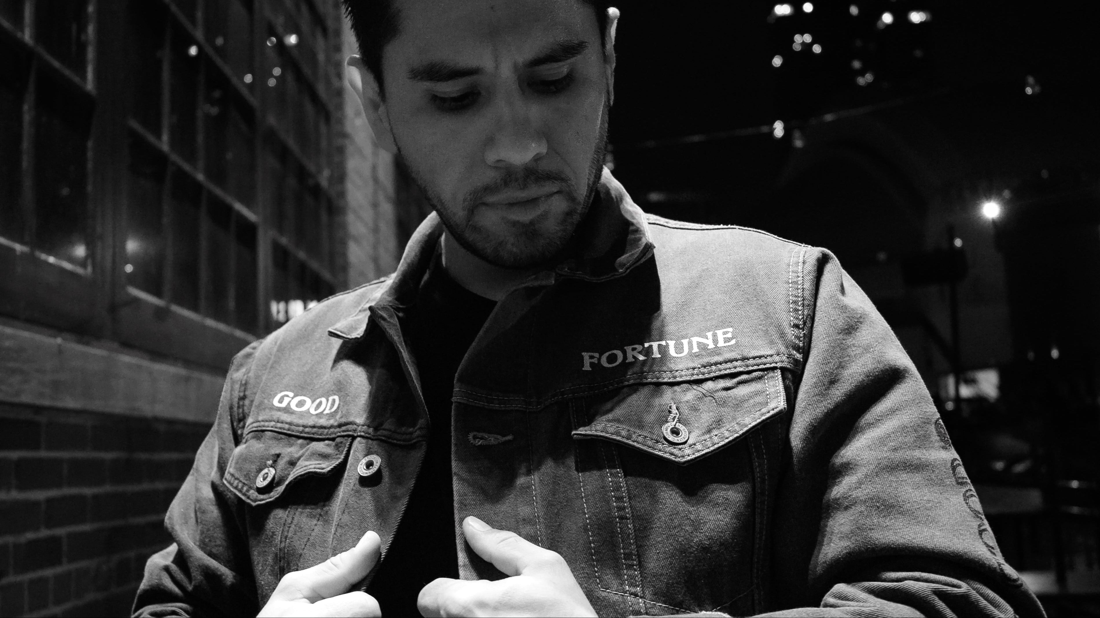 Man wearing a jacket with 'Fortune' branding, standing against an urban night background.